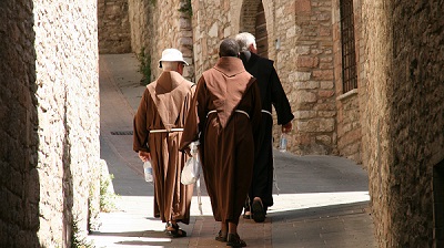 Tre brunkl�dda munkar vandrar bort�t, uppf�r en gr�nd i Assisi.