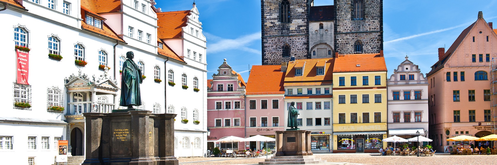 Staty av Luther mot medeltida bebyggelse och en klarblå himmel, i Wittenberg.